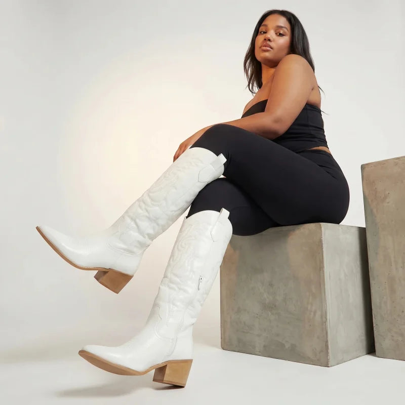 Model wearing Yehaw white vegan leather knee-high cowgirl boots with a pointed toe and medium block heel