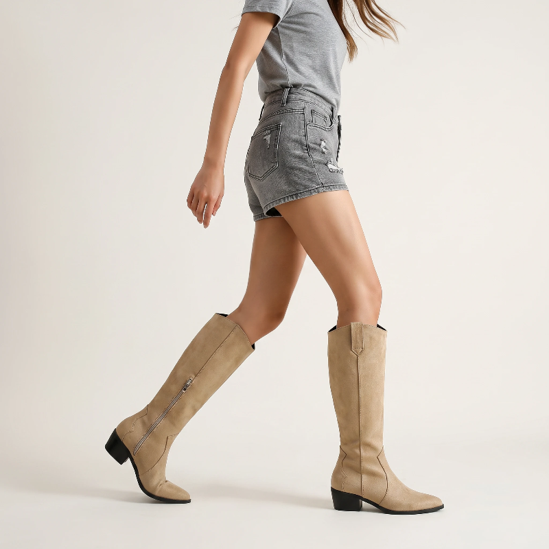 Yehaw beige vegan suede knee-high cowgirl boots with a pointed toe and side zip worn by a woman in denim shorts
