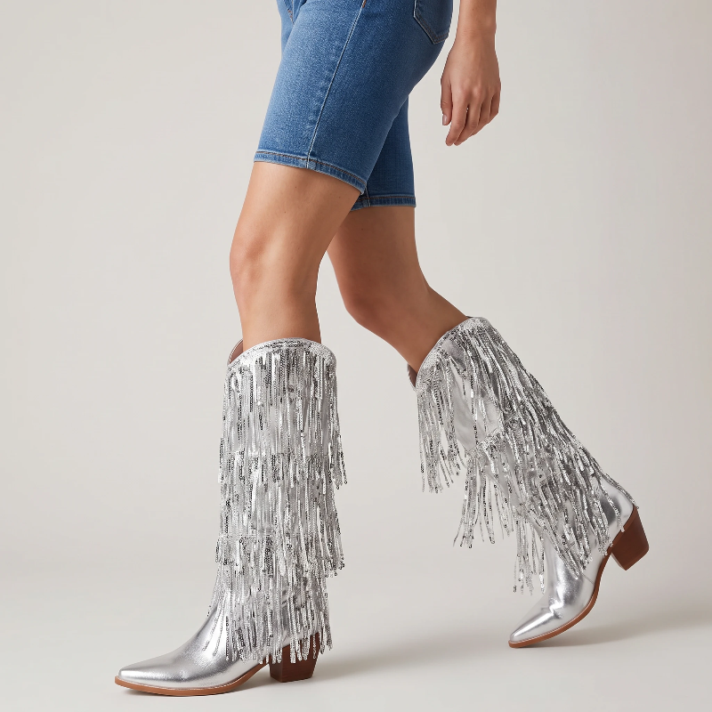Yehaw silver knee-high vegan leather cowgirl boots with metallic fringe detailing and a pointed toe.