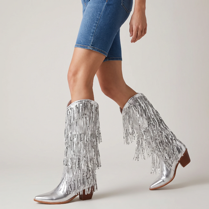 Yehaw silver knee-high vegan leather cowgirl boots with metallic fringe detailing and a pointed toe.