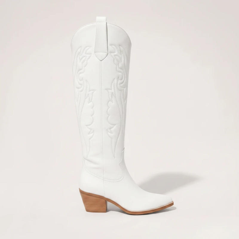 Model wearing Yehaw white vegan leather knee-high cowgirl boots with a pointed toe and medium block heel