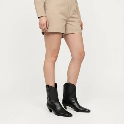 Yehaw BERTA black vegan leather ankle cowboy boots with a square toe and medium heel worn with beige shorts.