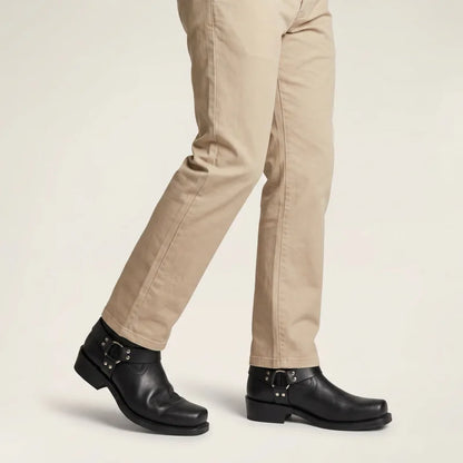 Yehaw black vegan leather cowboy boots with square toe, buckled strap, and high heel worn with beige trousers.