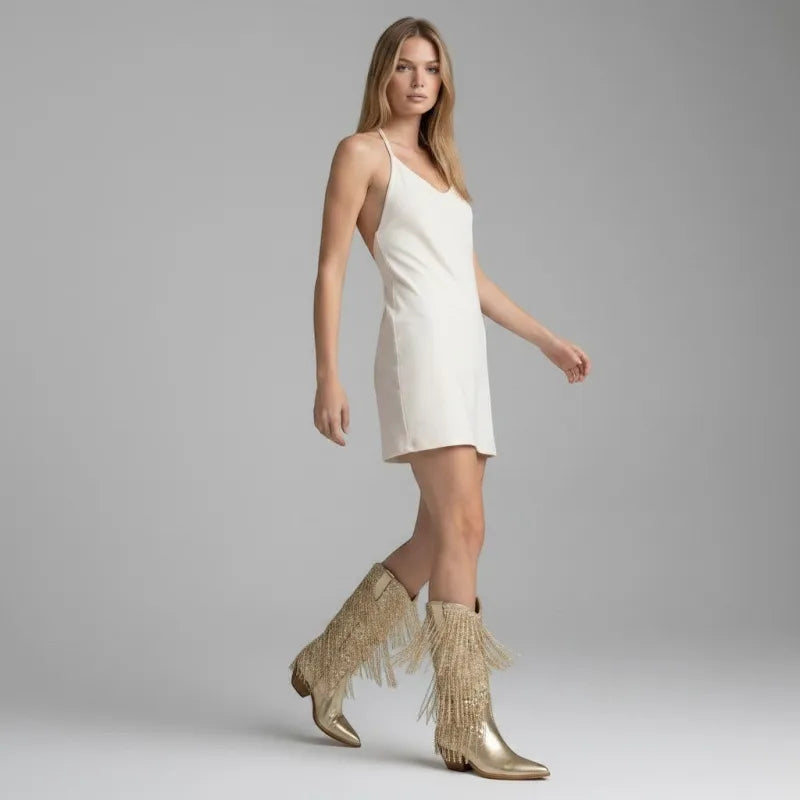 Yehaw gold vegan leather cowgirl boots with fringe and pointed toe, worn by a woman in a white dress.