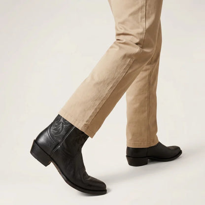 Yehaw black vegan leather cowboy boots with round toe and western stitching, worn with beige trousers.