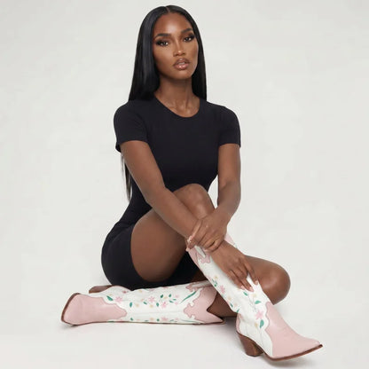 Model wearing Yehaw white and pink vegan leather knee-high cowgirl boots with floral embroidery and pointed toes.